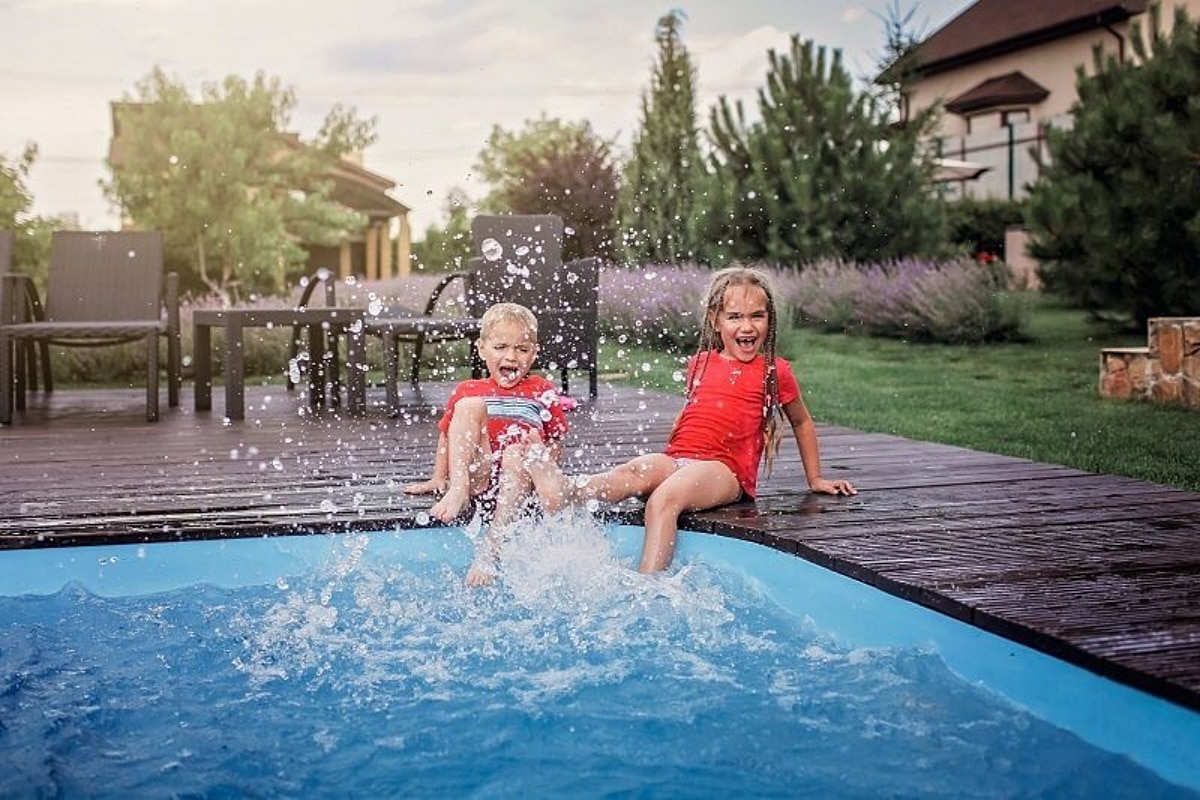 2 young girls sitting on the pool deck splashing, representing a family vacation home