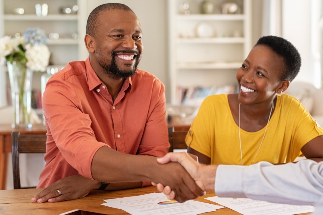 Happy African American couple. Man shaking hand of unseen man in a business setting. Representing setting up a Qualified Charitable Distribution (QCD)